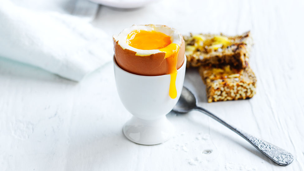 Boiled egg in a cup with a sppon and toast beside 