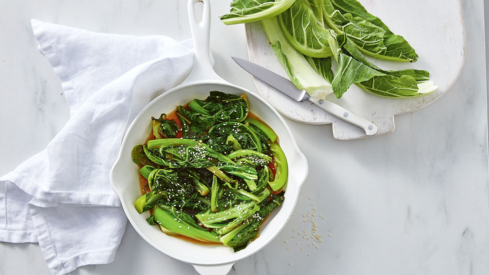 Cauliflower leaf stir-fry in a bowl, with a chopping board on the side with uncooked leaves