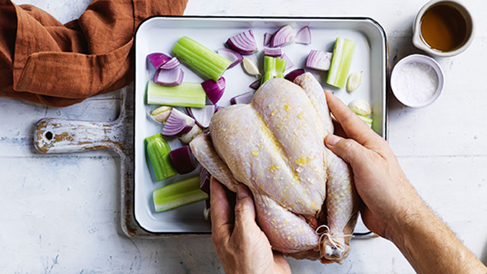 Uncooked chicken being placed on a baking tray with raw veggies