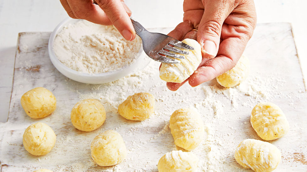 Hands making indents in gnocchi with a floured fork