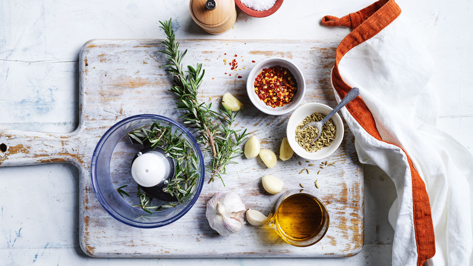 Rosemary, garlic, spices and olive oil displayed on a wooden board