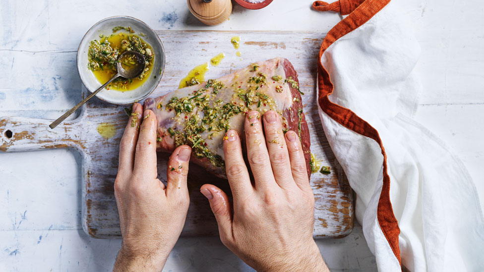 Marinade being rubbed on a lamb leg