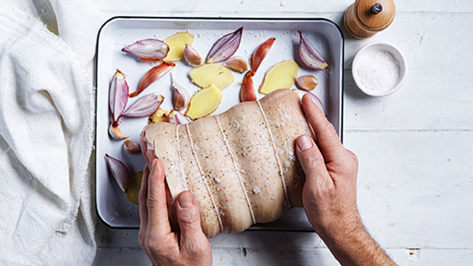 Uncooked pork being placed on a baking tray with veggies