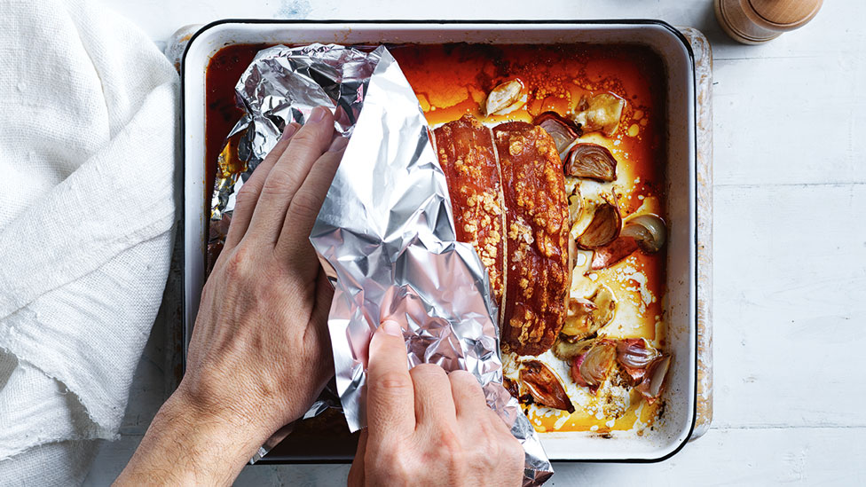 Roast pork with a person pulling tin foil off the baking dish