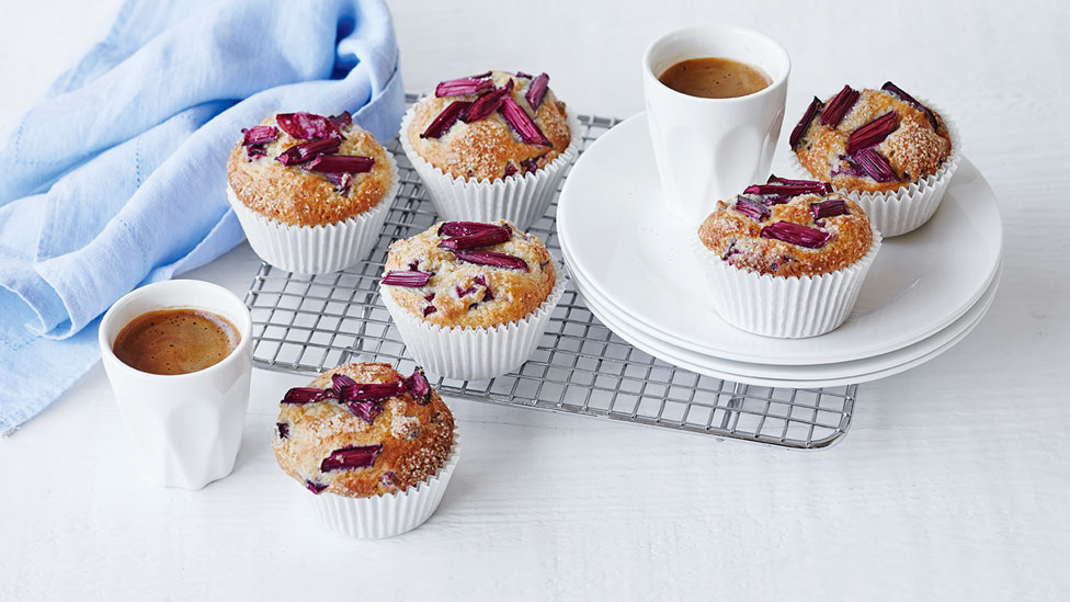 Rhubarb muffins on baking tray and plates and cups of hot drink