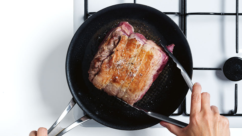 Meat in frying pan, hand holding the meat with tongs