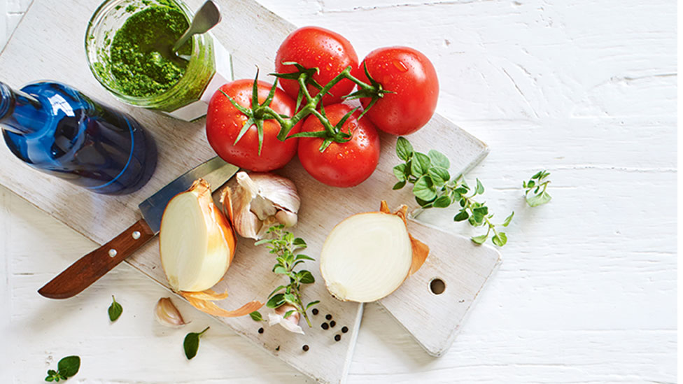 Tomatoes, pesto, garlic and onion with thyme sprig on a wooden shopping board