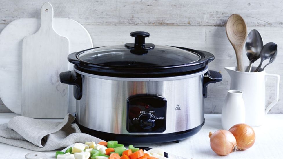 Slow cooker on a bench with vegetables in front of it.