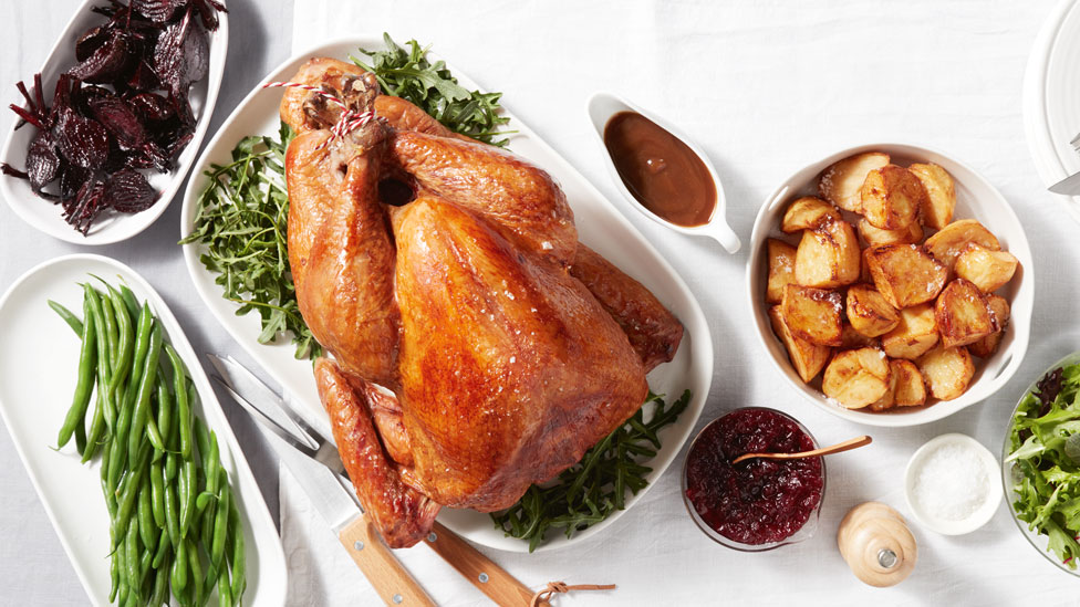 A whole roasted turkey with potato wedges and greens