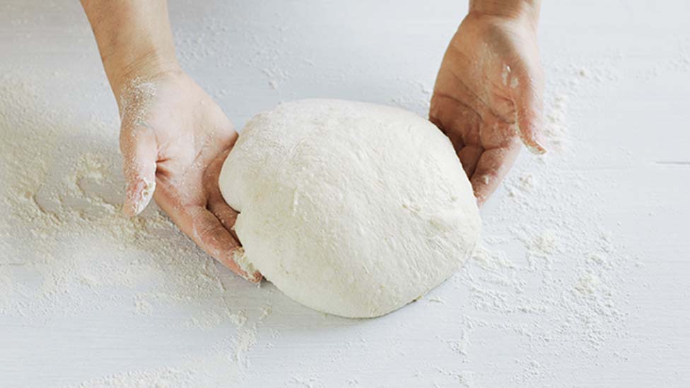 Two hands shaping the dough into a tight, neat ball