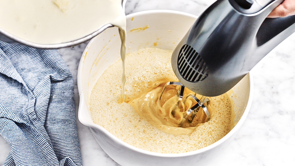 Pouring hot cream mixture into the egg yolk mixture while whisking