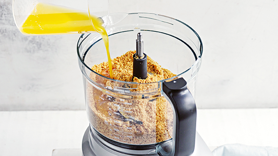 Butter being poured into a mixer with crushed biscuits