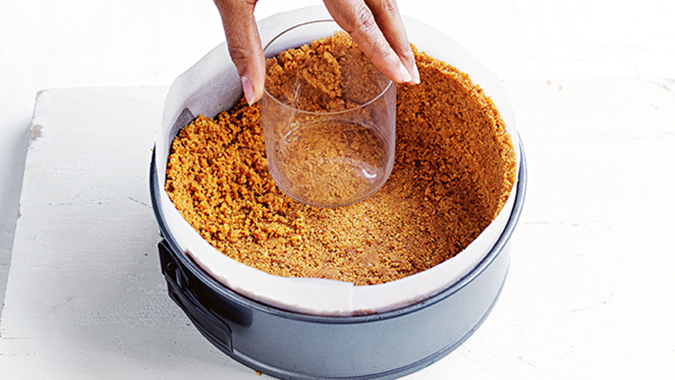 Person flattening biscuit crumbs into a cake tin to make a base