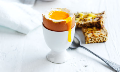 Boiled egg in a cup with sliced bread and spoon