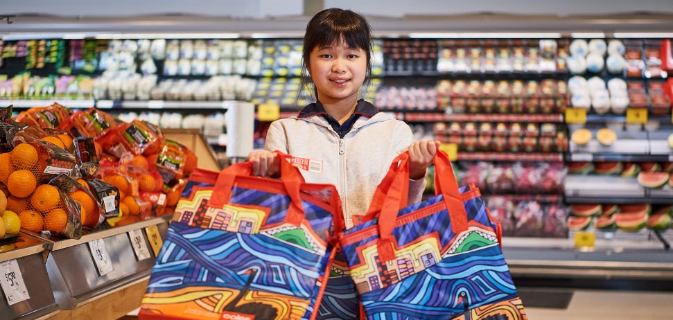 A girl holding two Coles reuseable bags in a Coles store
