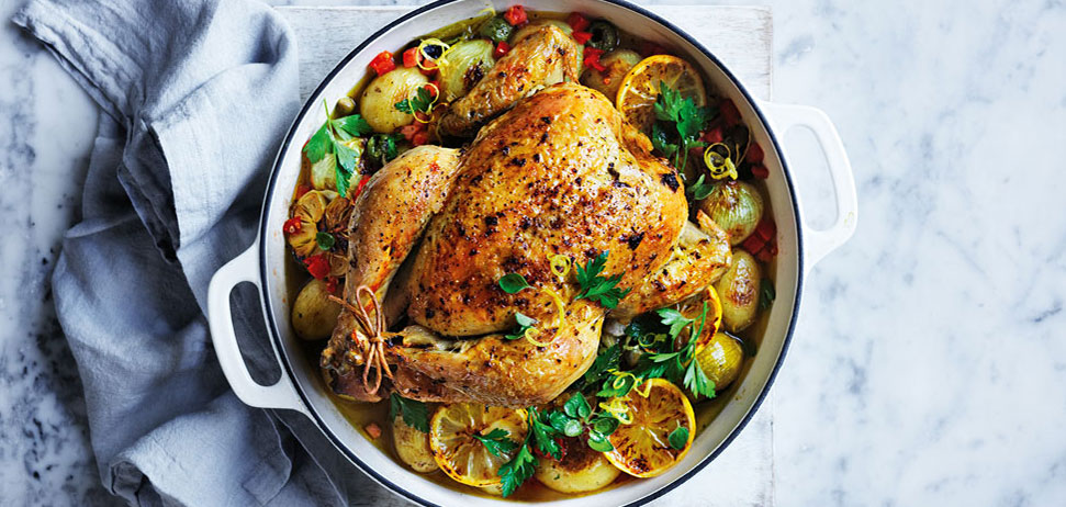 A whole golden brown roast chicken with assorted roast vegetables.