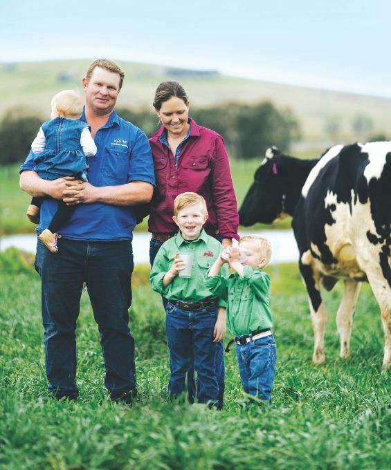 Family standing in a paddock with a cow, they are drinking glasses of milk