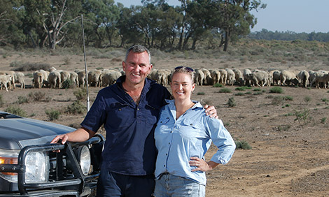 Paul and Nicole Fitzpatrick on their property with a herd of sheep in the background